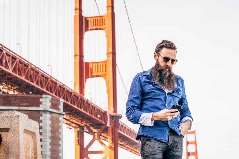 Bearded man checking his phone near the Golden Gate Bridge tower in San Francisco