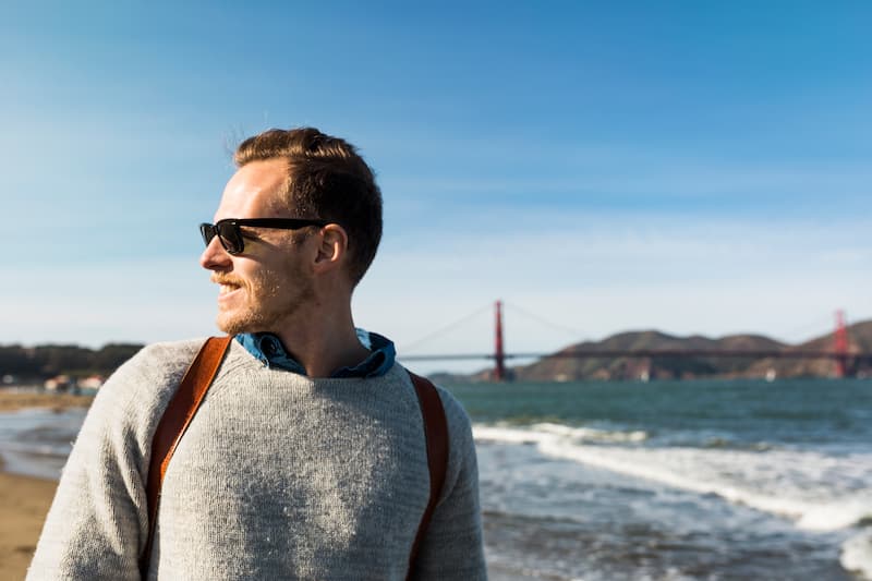 Man smiling and looking toward the Golden Gate Bridge from a San Francisco beach